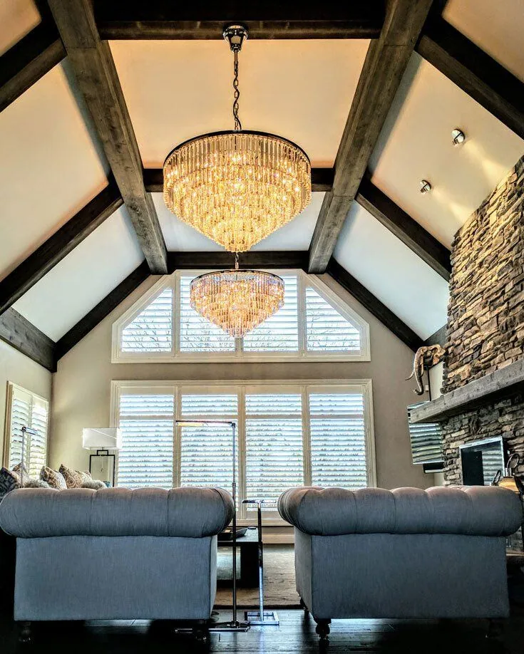 A great room with a vaulted beamed ceiling, a crystal chandelier and white shutters on the windows