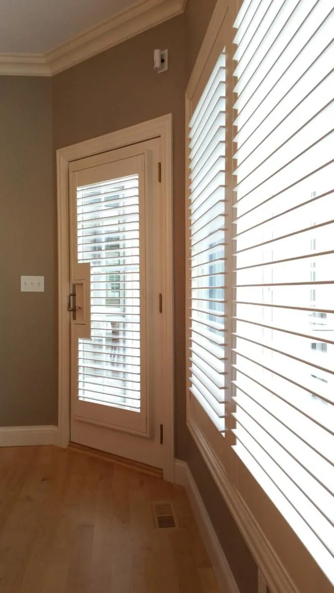 A plantation shutter on a swing door, cut around the handle, beside a wall of shuttered windows