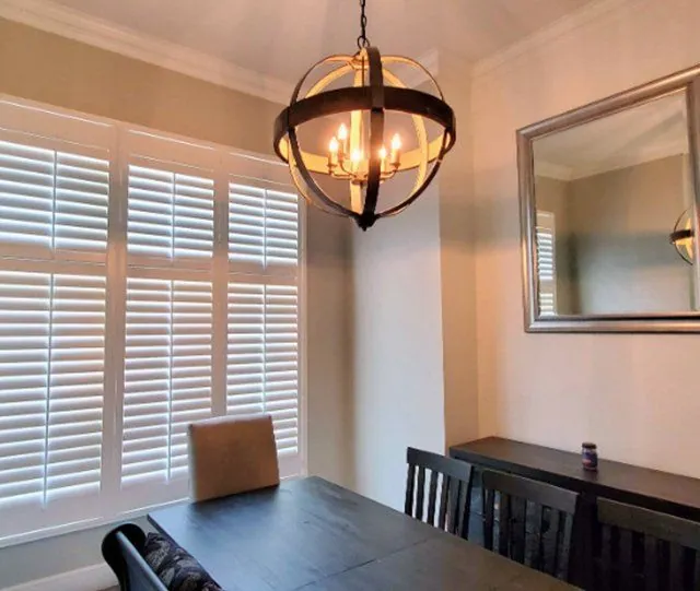 White plantation shutters in a dining room with a round chandelier