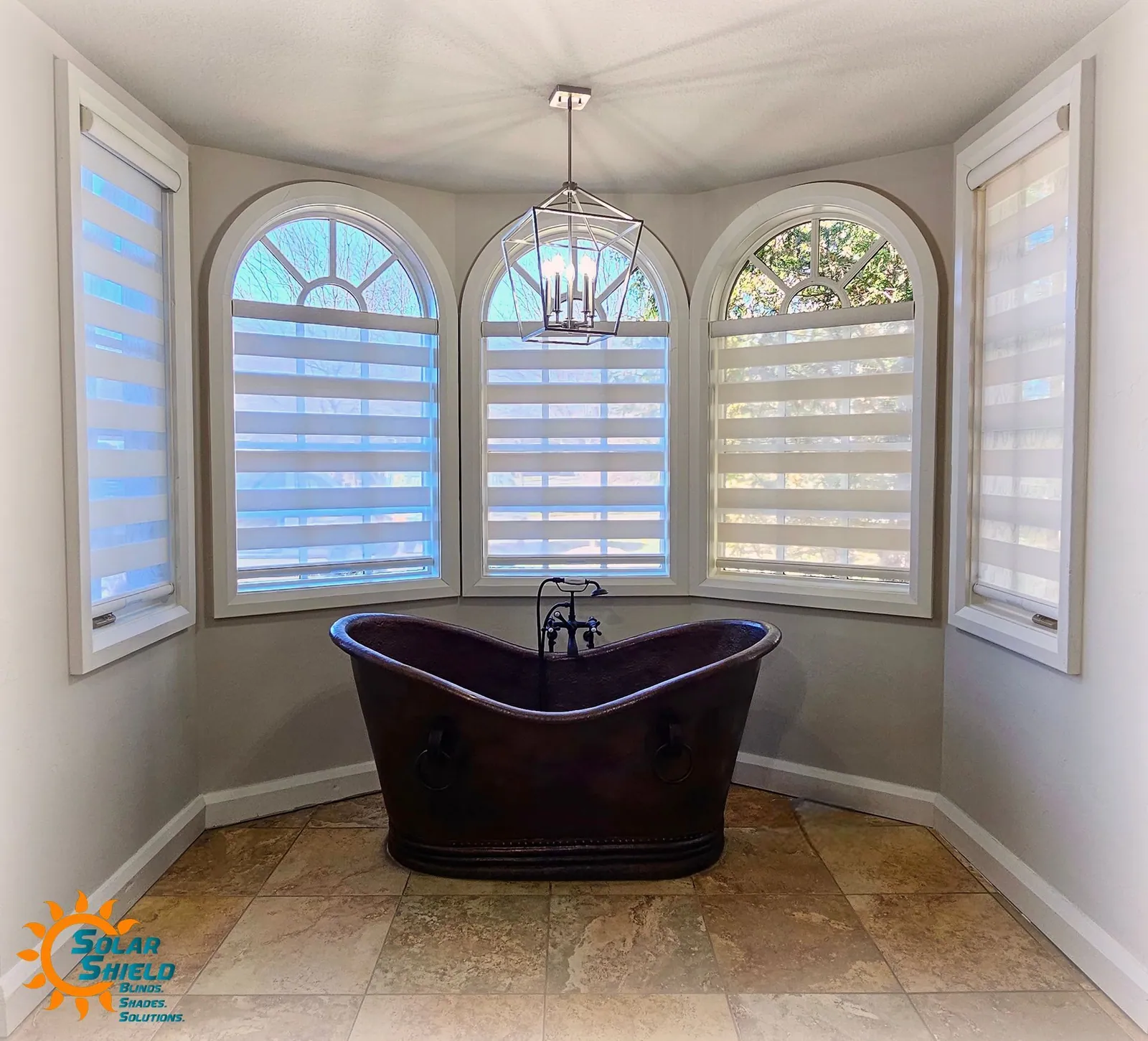 Banded shades on arched bay windows around a freestanding tub, installed by Solar Shield Blinds