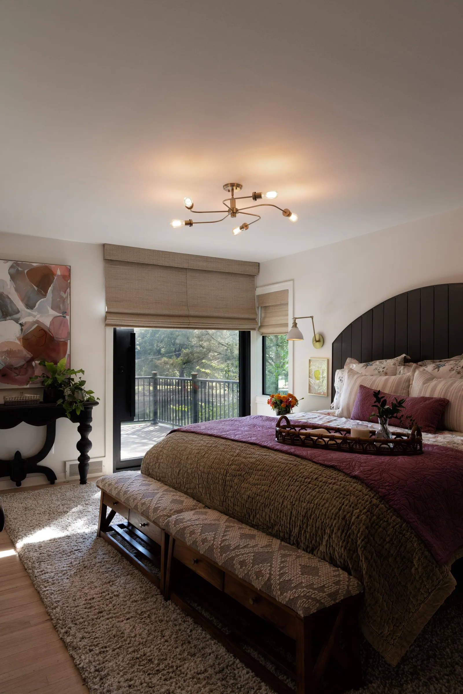 Natural woven shades on the windows of a primary bedroom behind a bench and bed, installed by Solar Shield Blinds