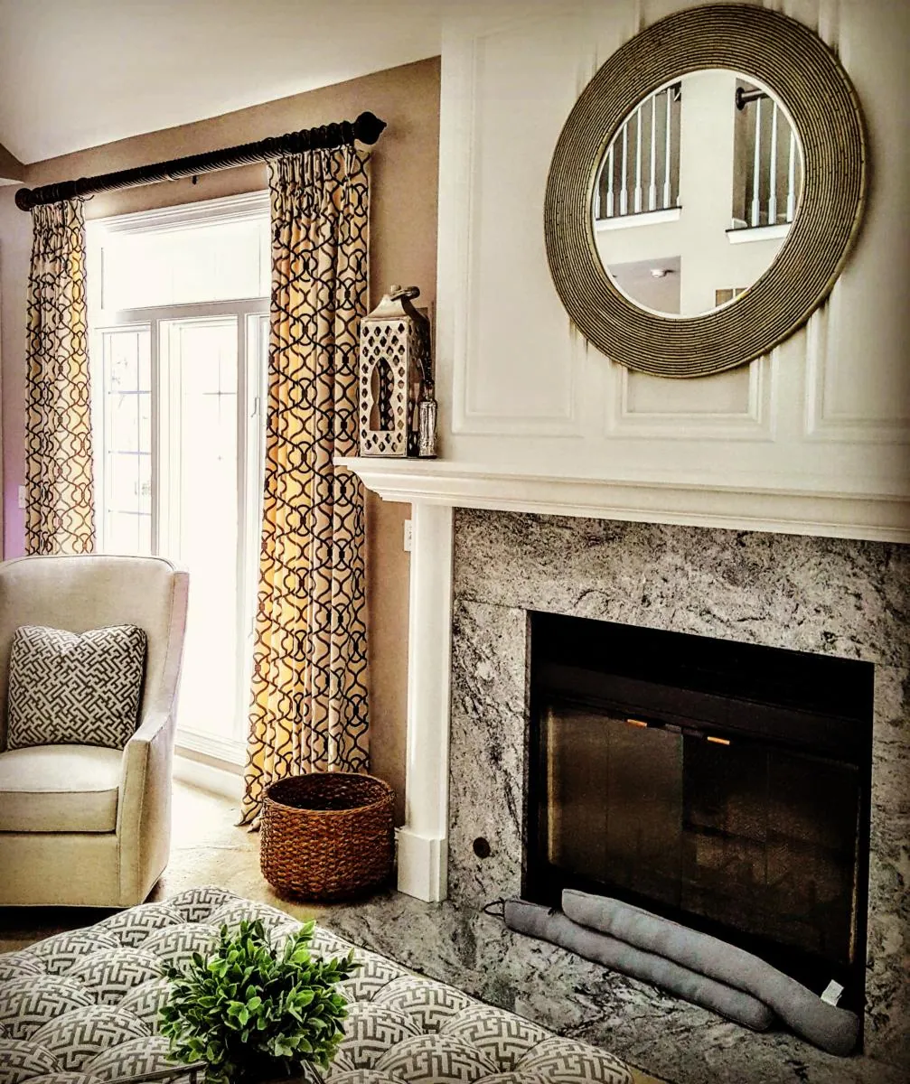 Patterned drapery panels on a rod beside a fireplace and round mirror, installed by Solar Shield Blinds