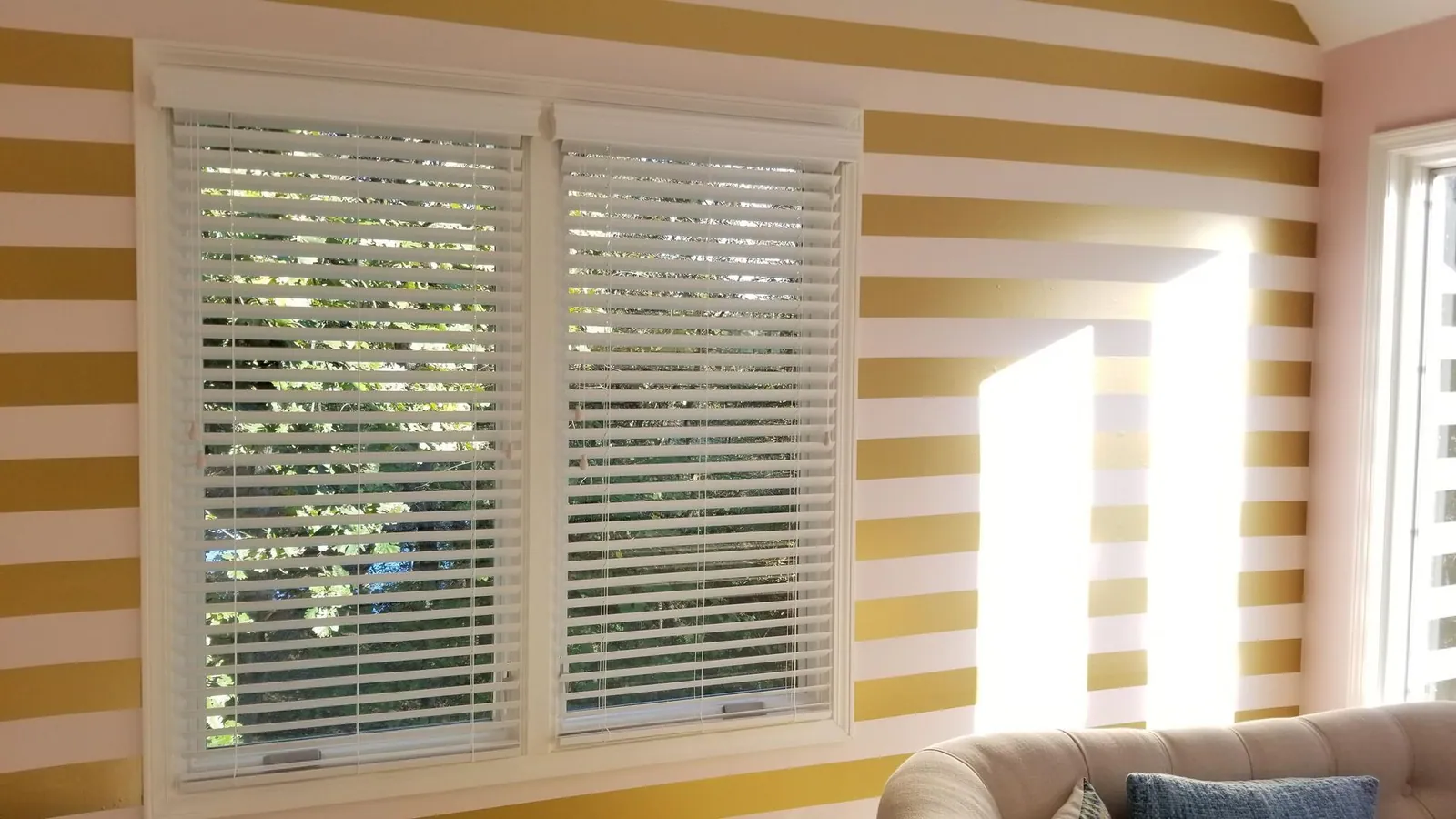 White wood blinds on a pair of windows in a room with a striped wall