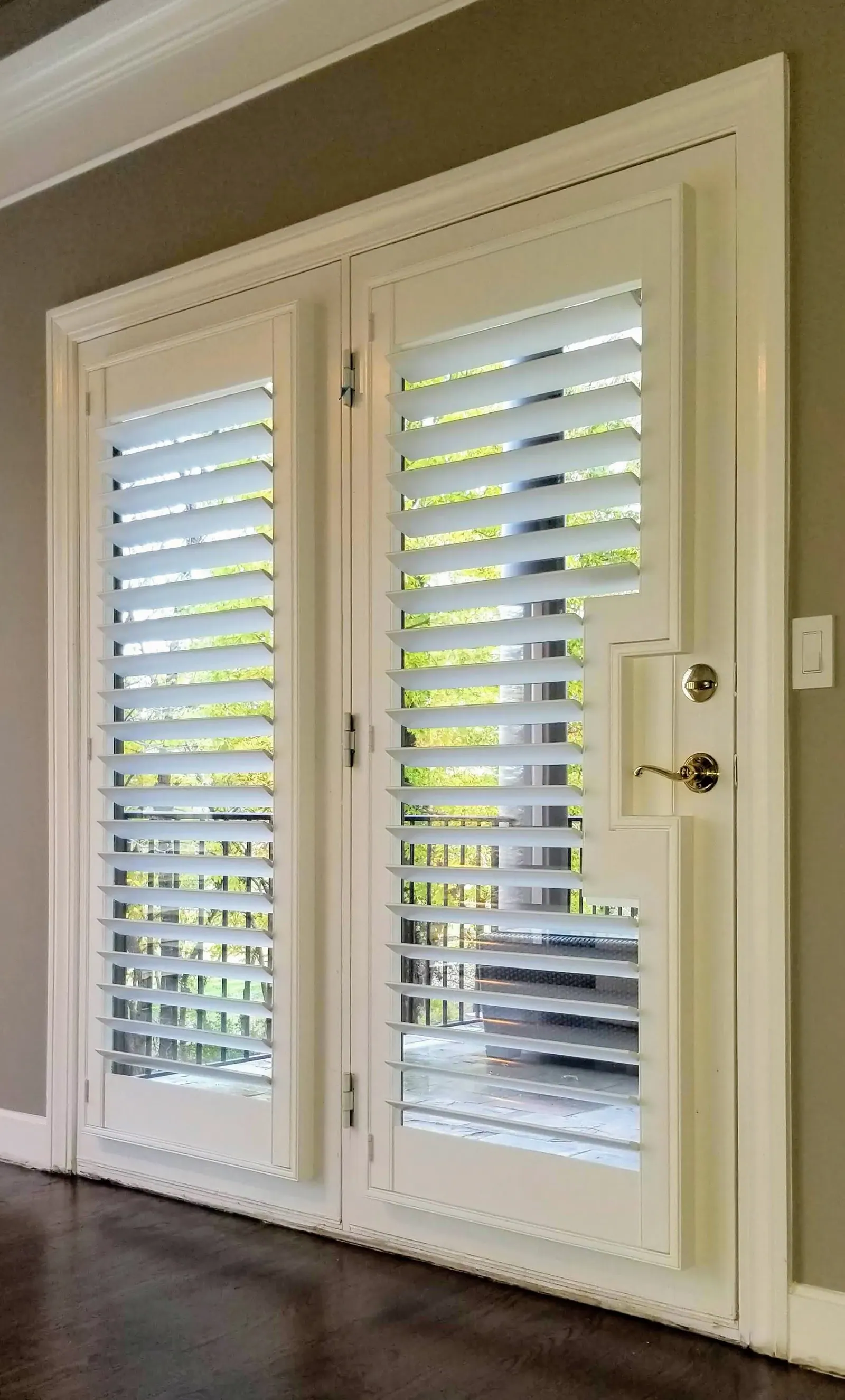 Plantation shutter on a French door, louvers open, with the cutout around the lever handle