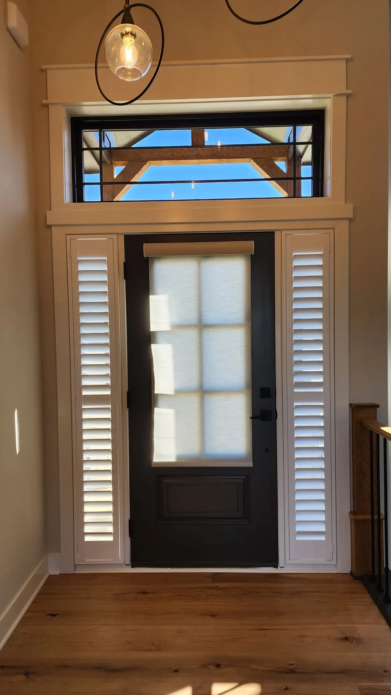 Honeycomb shade on a dark front door with shuttered sidelights and a transom above