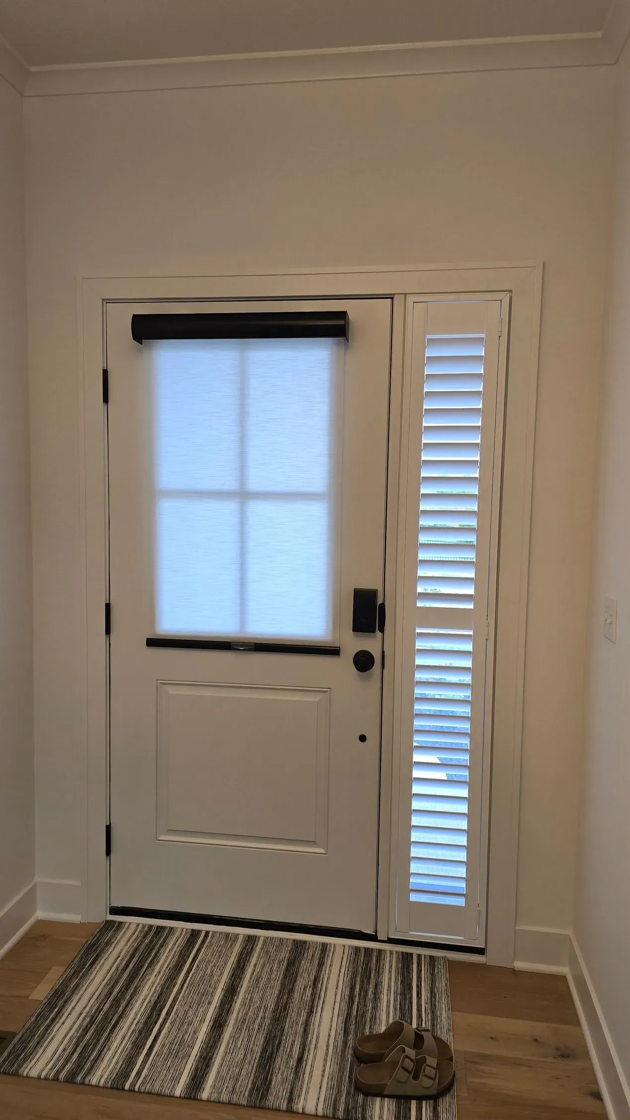 Roller shade on a white front door with a plantation shutter on the sidelight