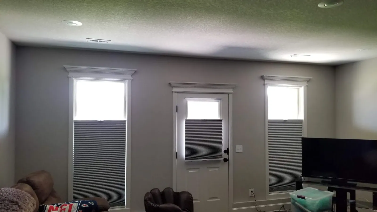 Honeycomb shades lowered from the top on the windows and swing door of a media room