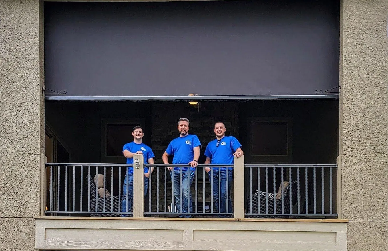 Three Install Techs in blue Solar Shield Blinds shirts on a balcony under a lowered exterior shade
