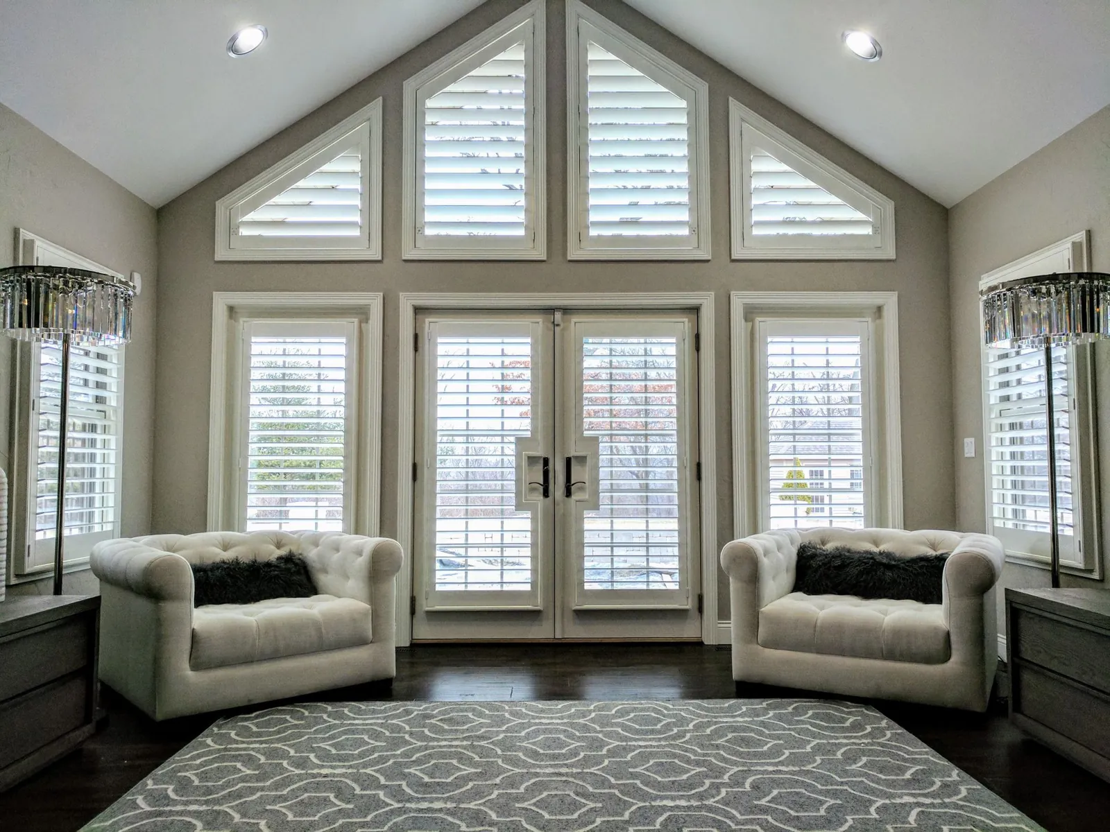 A full wall of plantation shutters across French doors, side windows and the arched transoms above