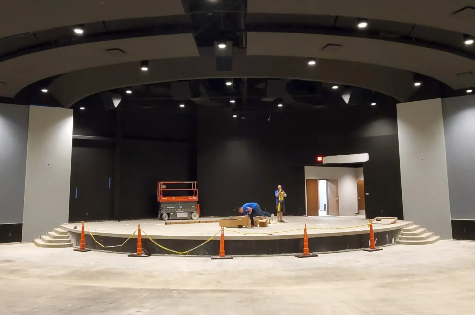 The bare church platform before the curtains, with black walls, a scissor lift and caution cones