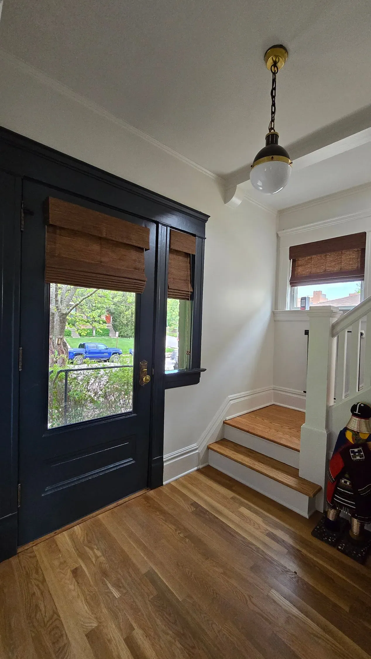 Natural woven shades on a dark front door and the window beside the stairs