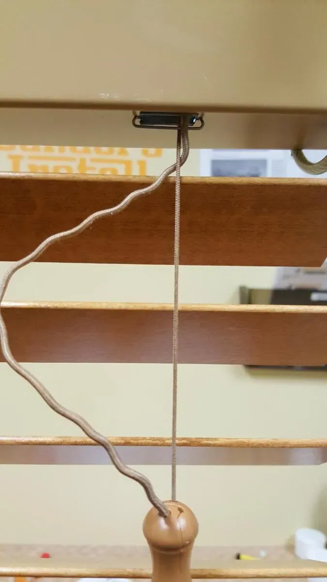 A broken lift cord hanging from a wood blind headrail