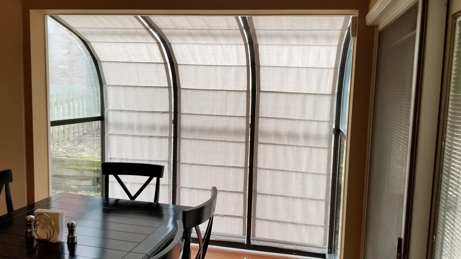 Light filtering shades following the curve of sunroom glass above a dining table