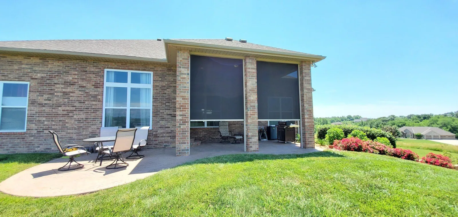 Brick home with the patio shades half lowered, installed by Solar Shield Blinds