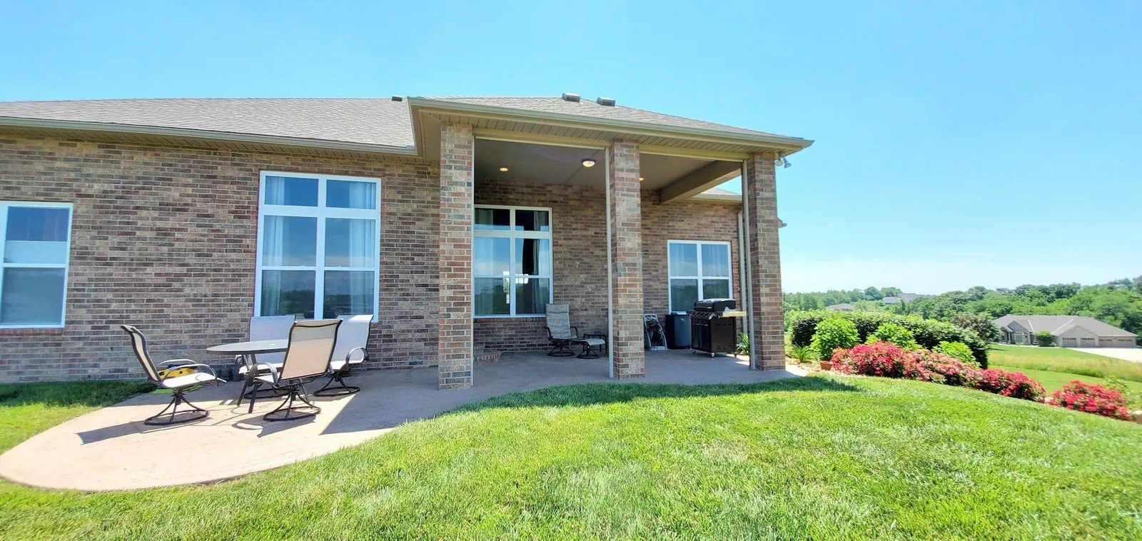 Brick home with both patio shades raised and the dining set on the slab, installed by Solar Shield Blinds