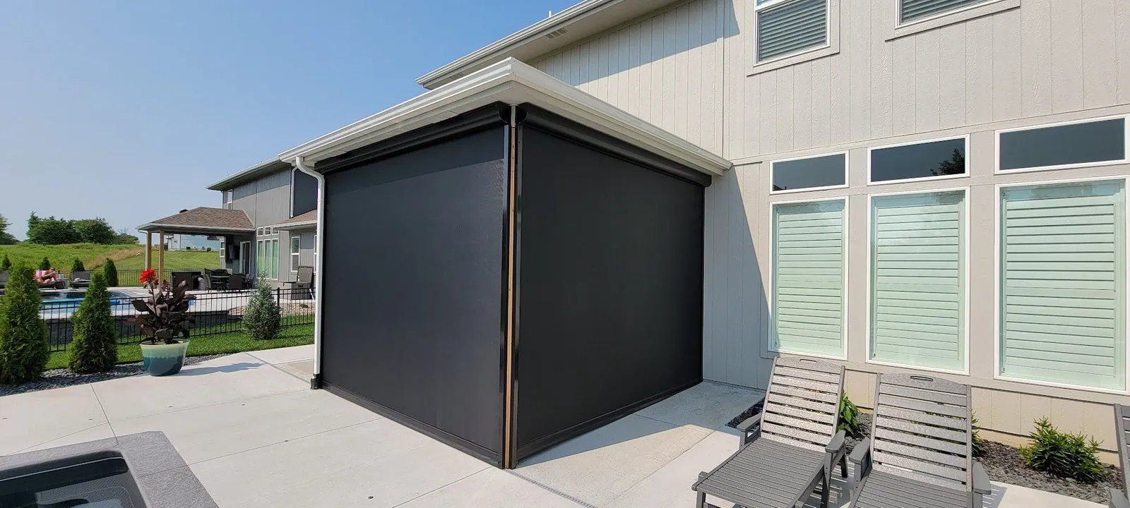 Dark screen lowered on a covered patio, seen from the side with a lounger in front, installed by Solar Shield Blinds