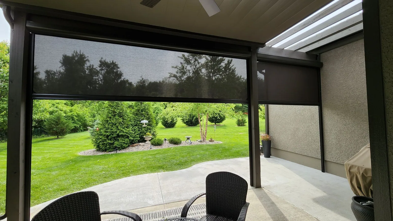 Patio with dark screens lowered and wicker chairs at the table, installed by Solar Shield Blinds