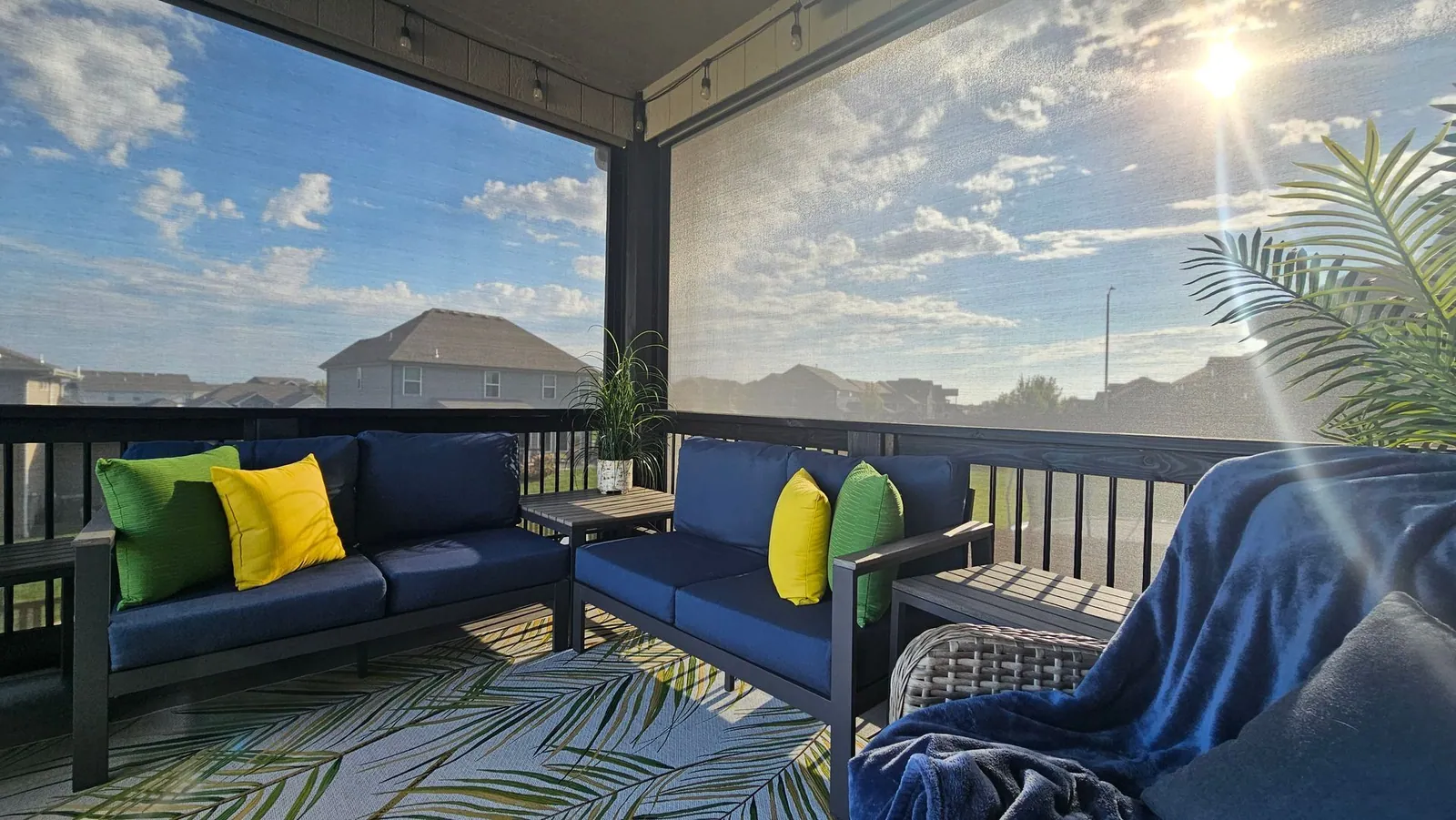 A deck sectional with yellow and green pillows behind lowered screens, the morning sun coming through