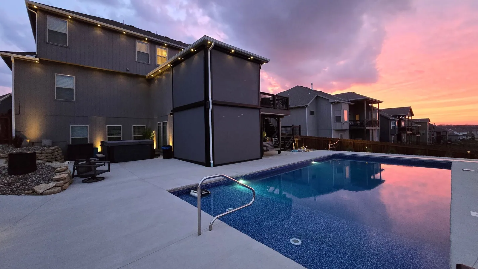Exterior patio shades lowered on a pool deck at sunset, the house lit behind them