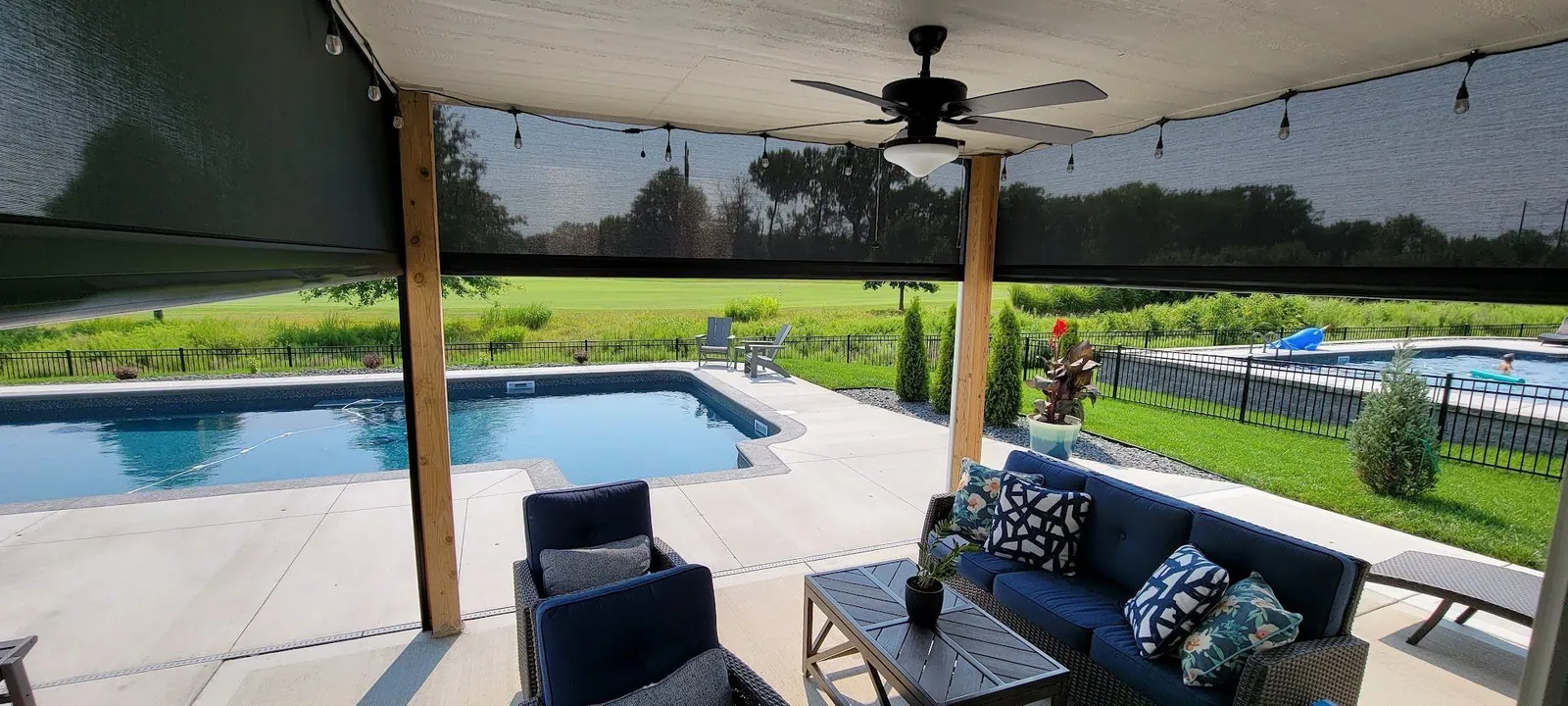 Patio seating behind lowered screens with the pool in the background, installed by Solar Shield Blinds