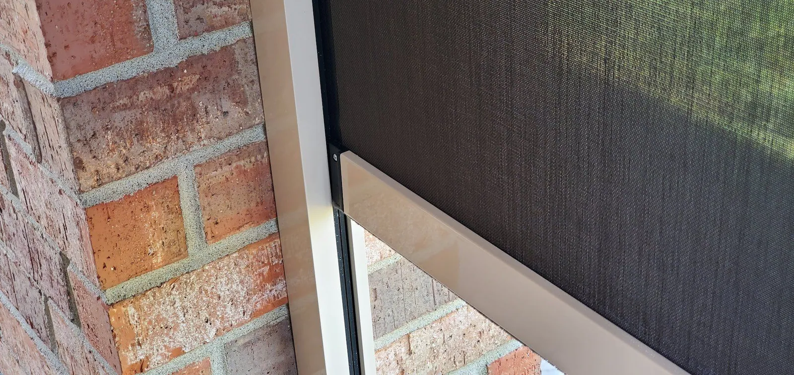 Close up of the screen fabric and bottom rail against a brick column, installed by Solar Shield Blinds