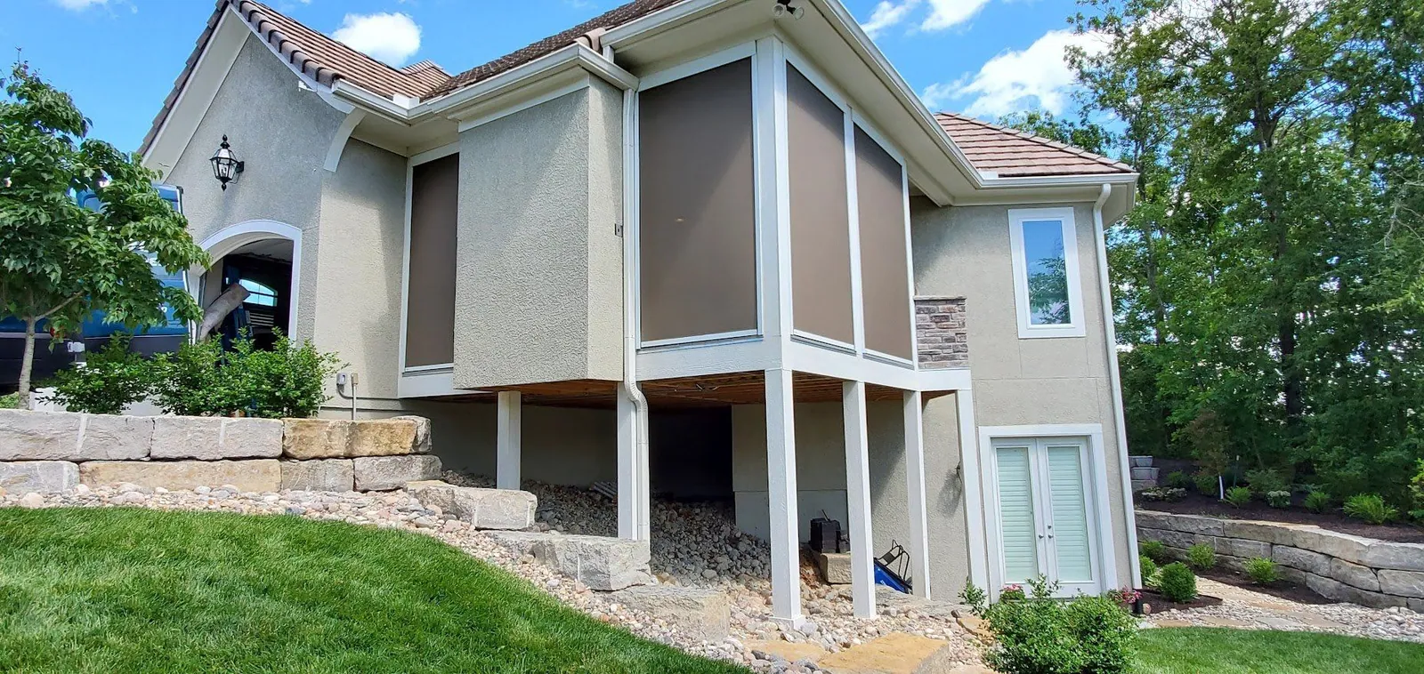 Stucco home with exterior shades lowered on both the upper deck and the lower patio, installed by Solar Shield Blinds