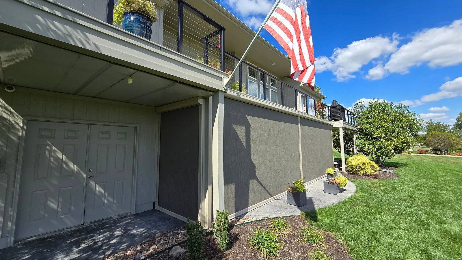Under deck patio with the screens lowered and a flag flying above, installed by Solar Shield Blinds