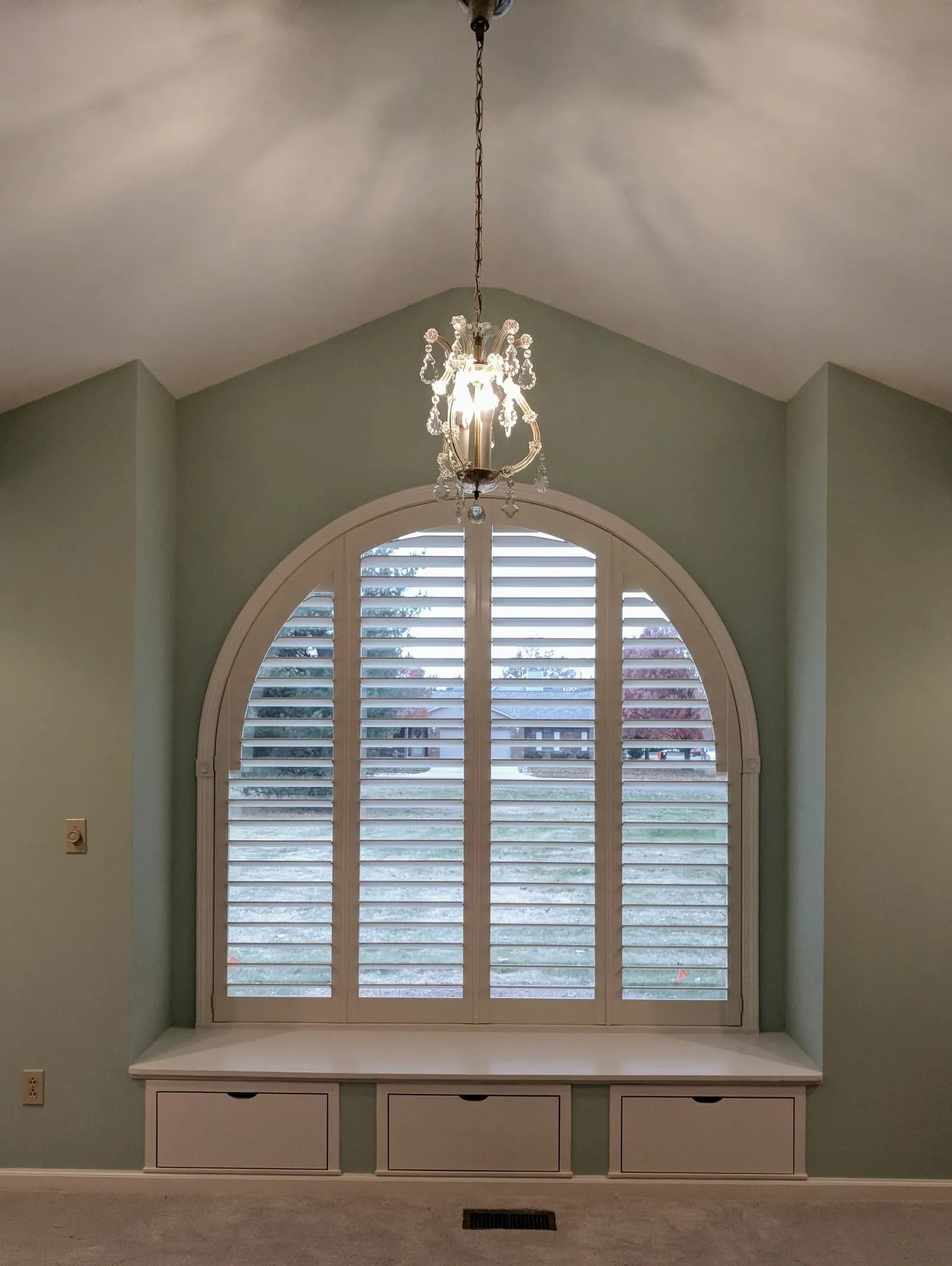 Arch top plantation shutter above a window seat under a vaulted ceiling