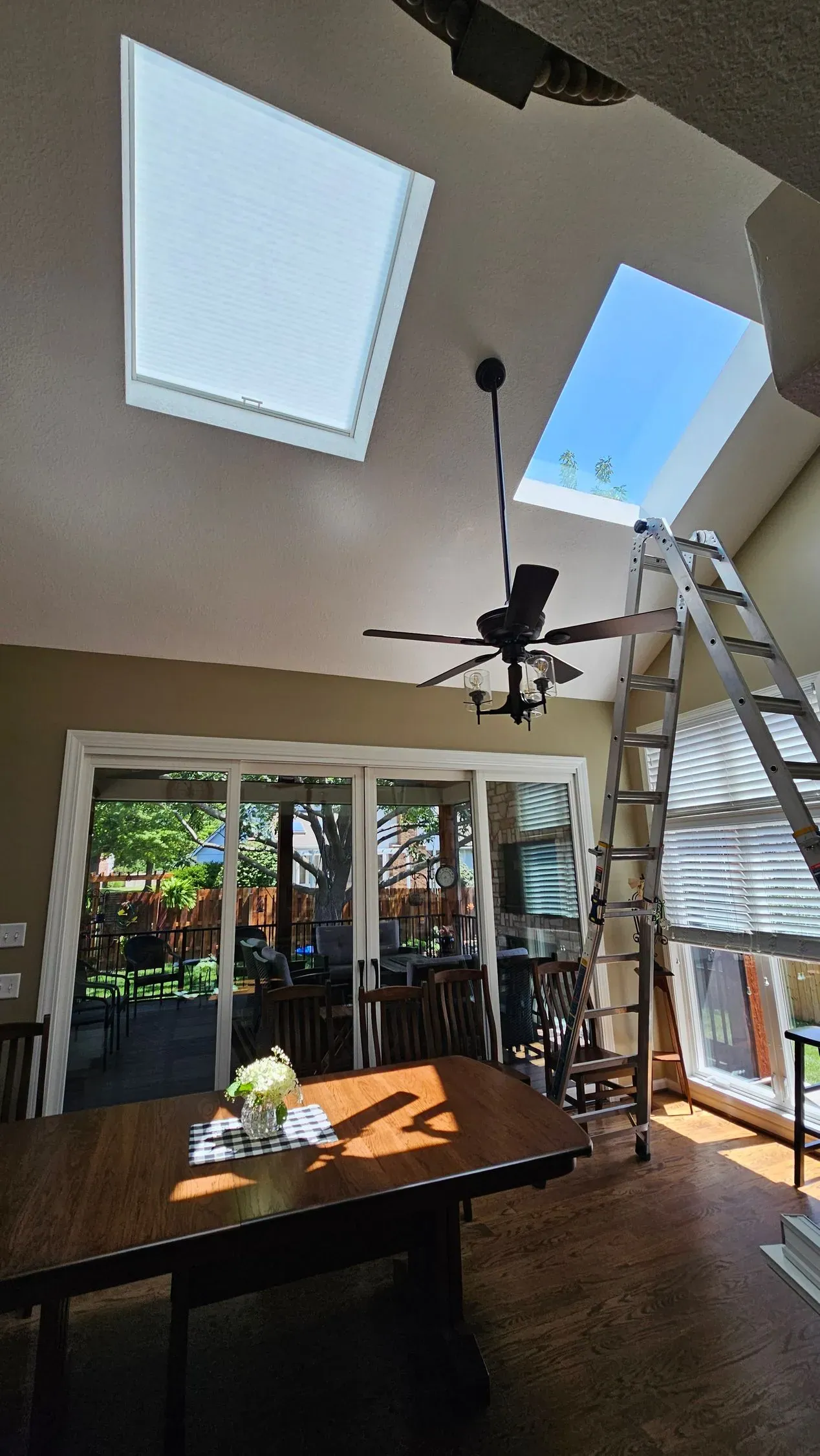 A vaulted dining room with one skylight covered by a Honeycomb Shade, the second still open, and an install ladder in place
