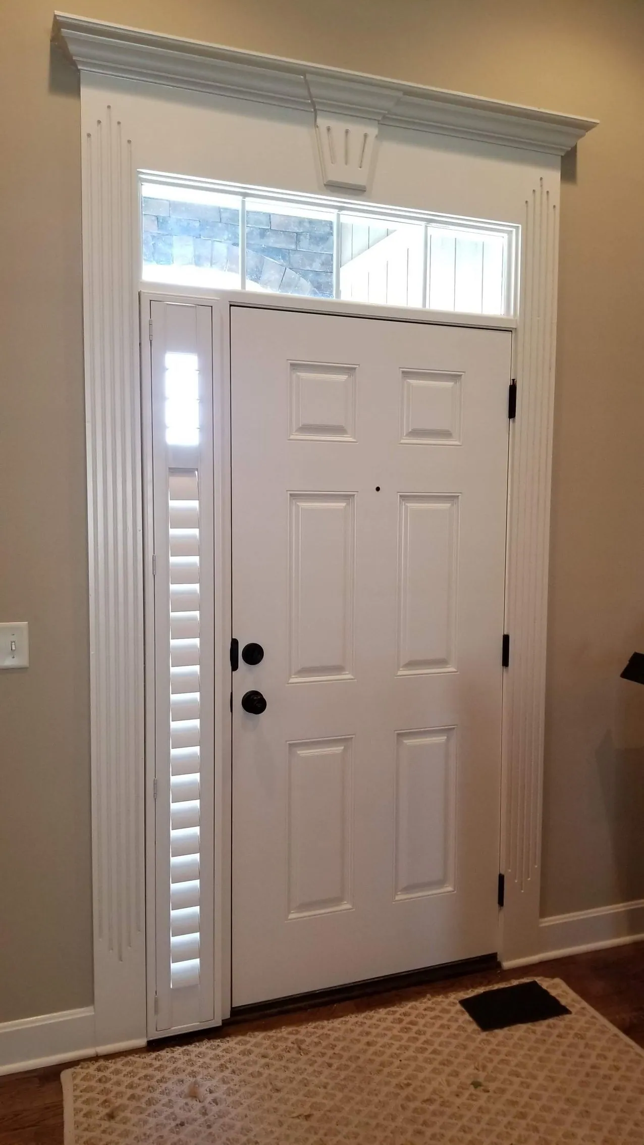 A shuttered sidelight beside a six panel door, with the transom above