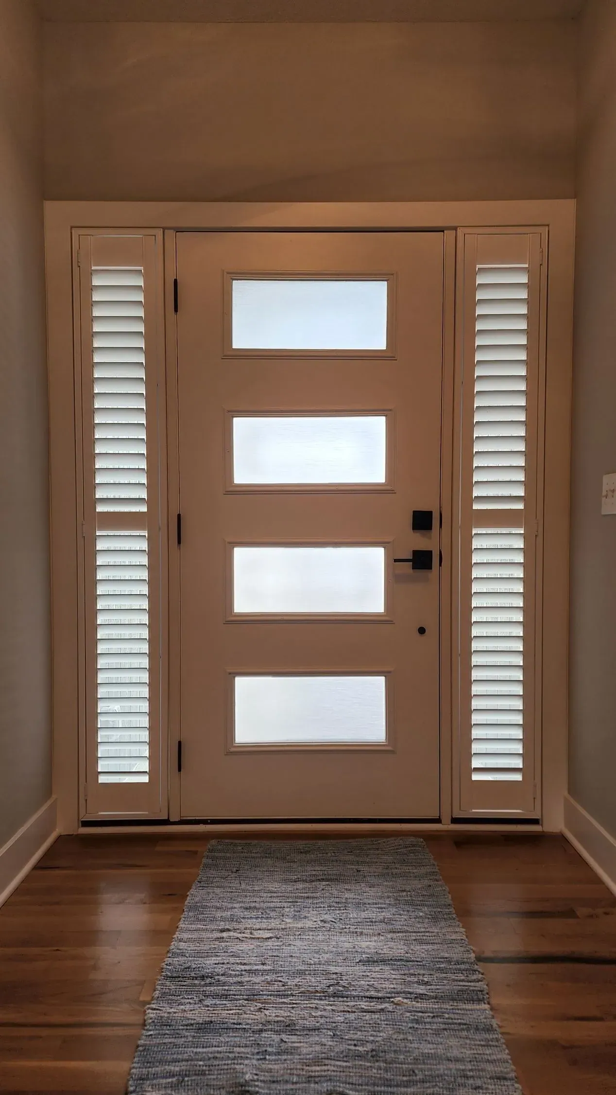 Plantation Shutters on both sidelights of a modern front door with frosted glass panels