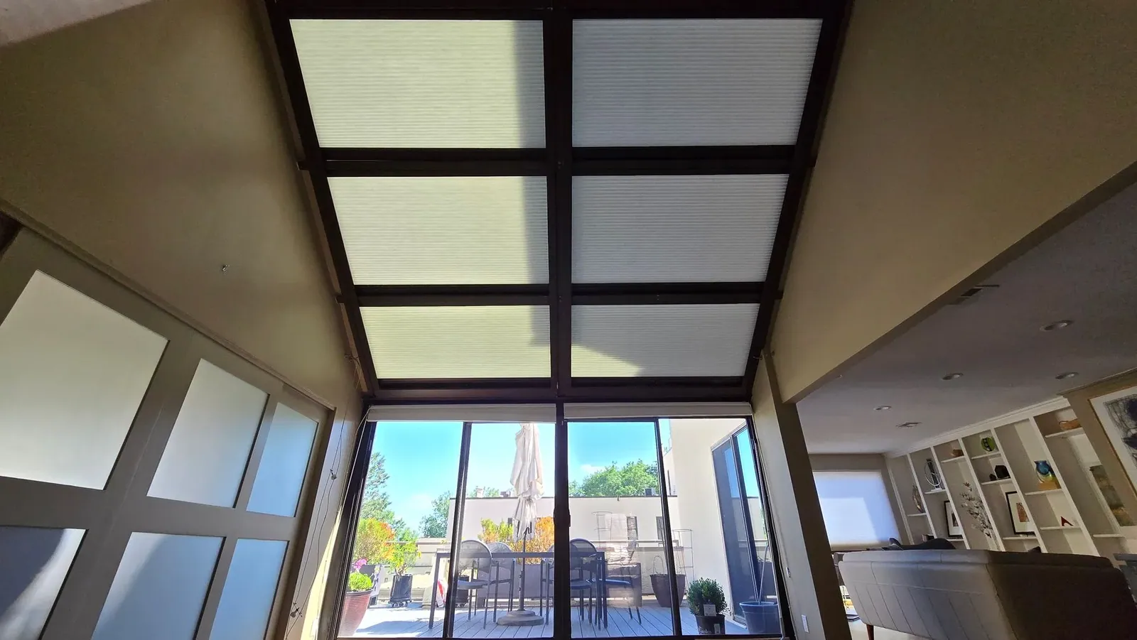 Six motorized Honeycomb Shade panels lowered together across a dark framed skylight above a sitting room