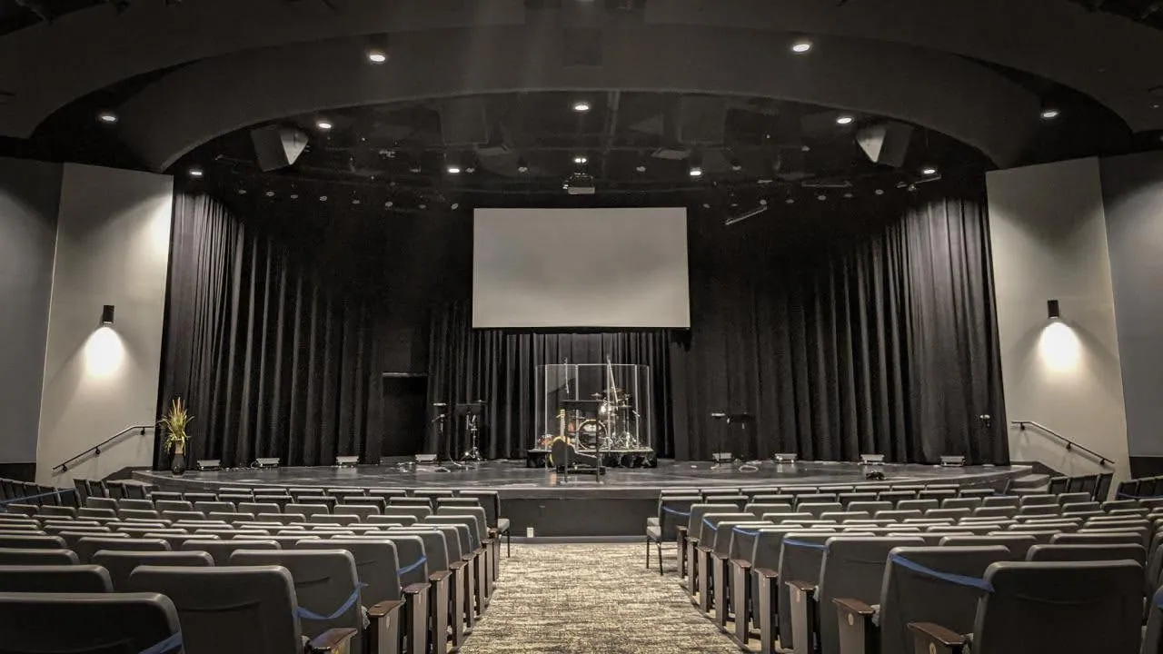 A church auditorium with black stage curtains across the back wall and a projection screen above the platform