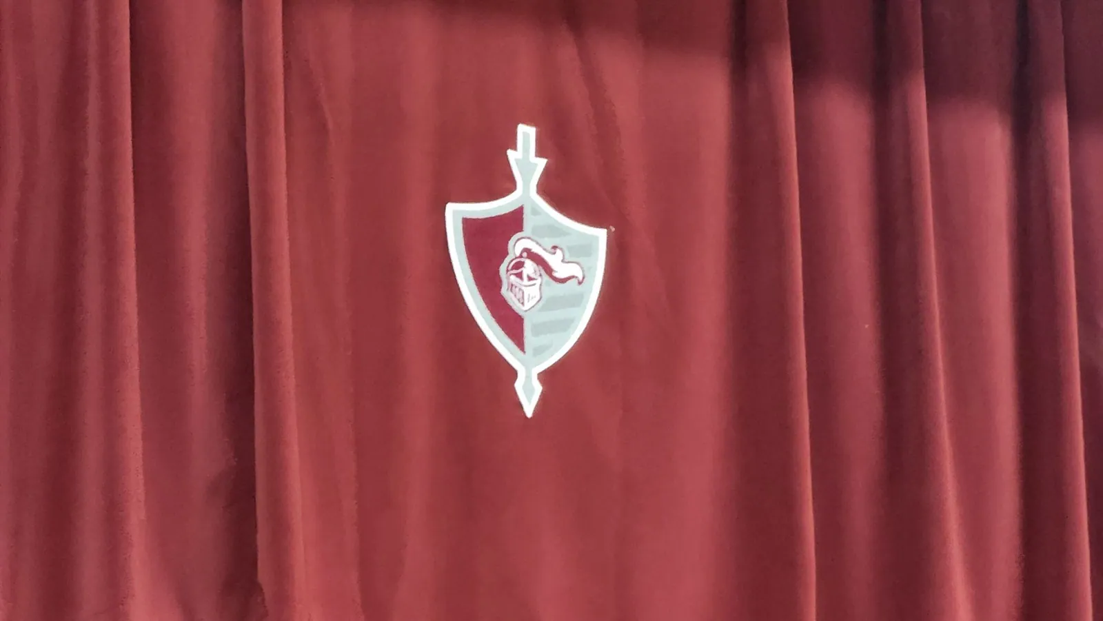 A custom school crest sewn onto a red stage curtain valance