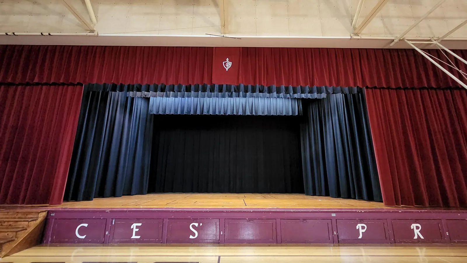 A wide view of a gymnasium stage with a red valance, a blue border and black legs