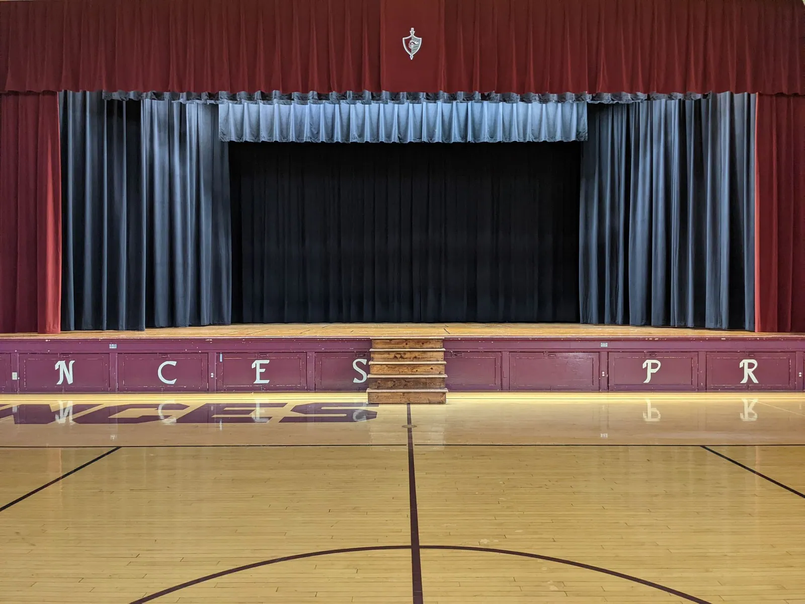 A gymnasium stage with a maroon valance and side curtains, a blue border and a black rear curtain