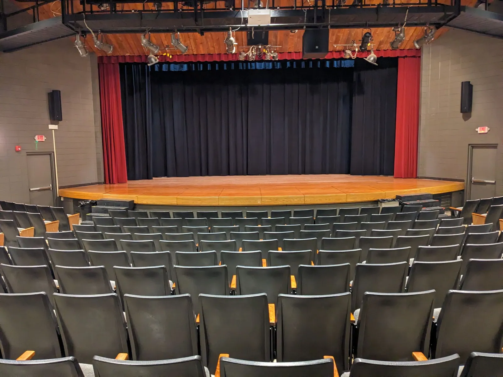 A school theater stage with a red valance, red side curtains and a black front curtain, seen from the seating