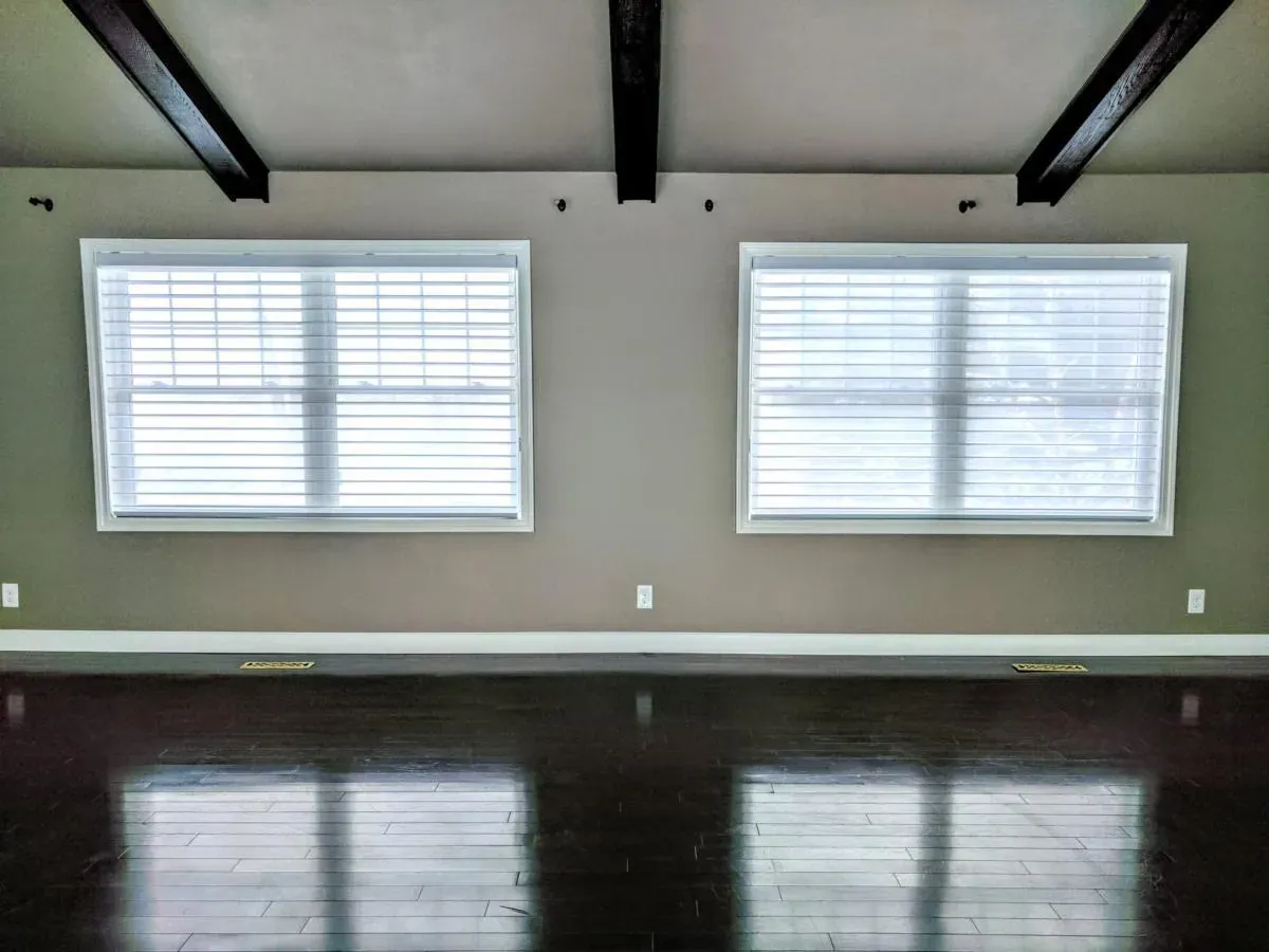 White blinds on two windows in an empty room with a dark wood floor