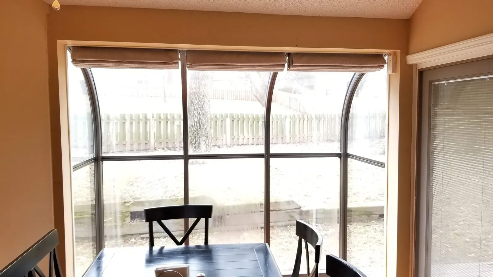 Light filtering shades on curved sunroom glass, seen from the dining table