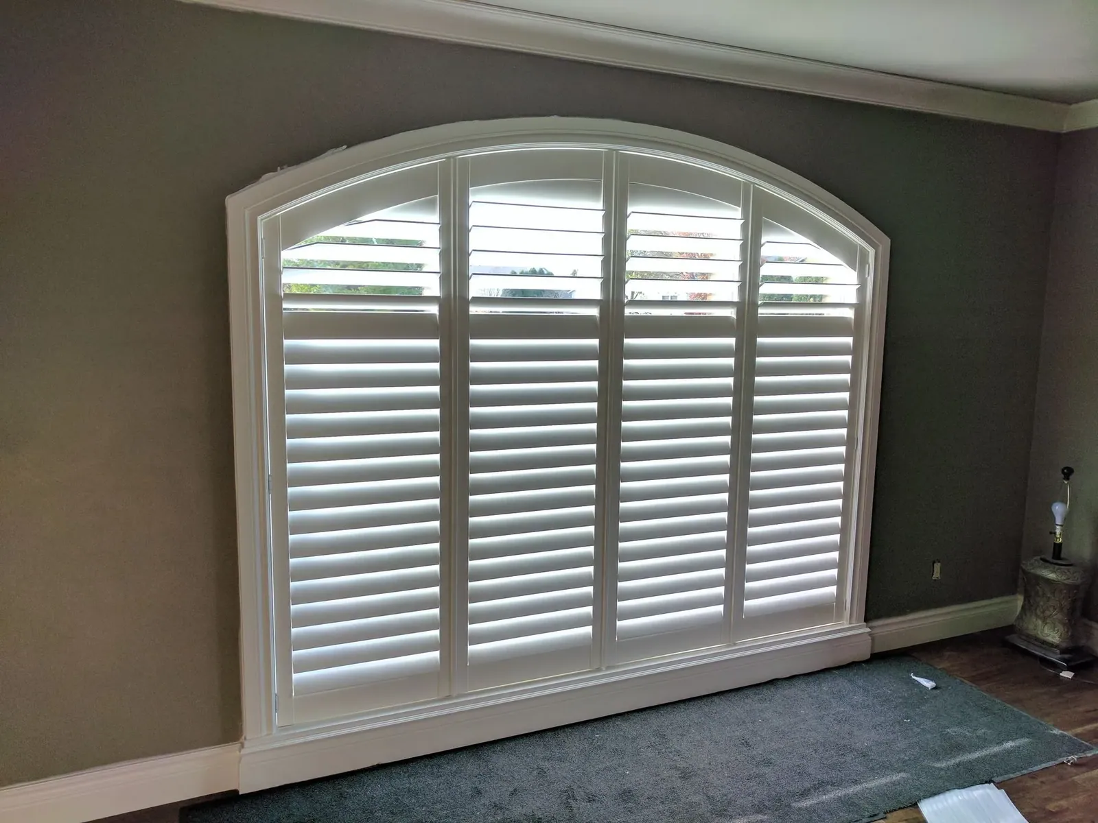 Arch top plantation shutter with the louvers open in a gray room